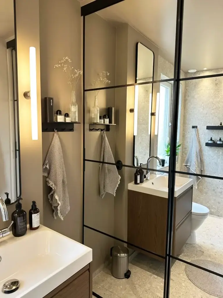 Lyxigt badrum i Bromma med spegelvägg, kommod och dusch i steninspirerad stil.