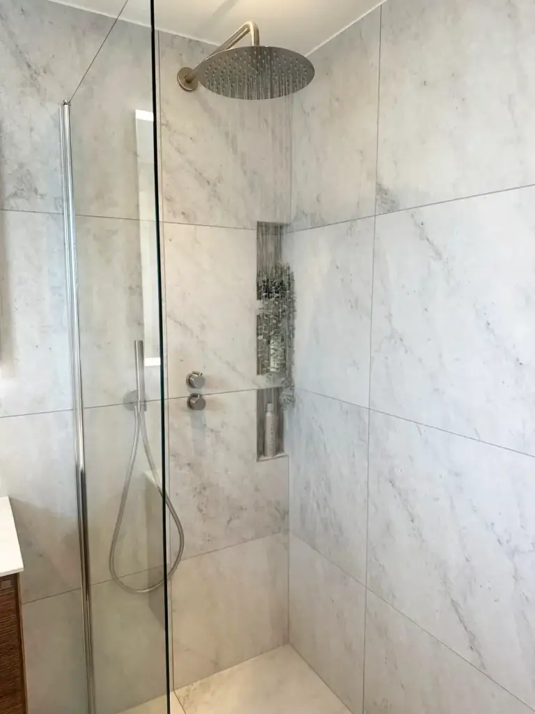 Elegant takdusch i krom med stora kakelplattor i naturstenslook i badrumsrenovering Bromma.