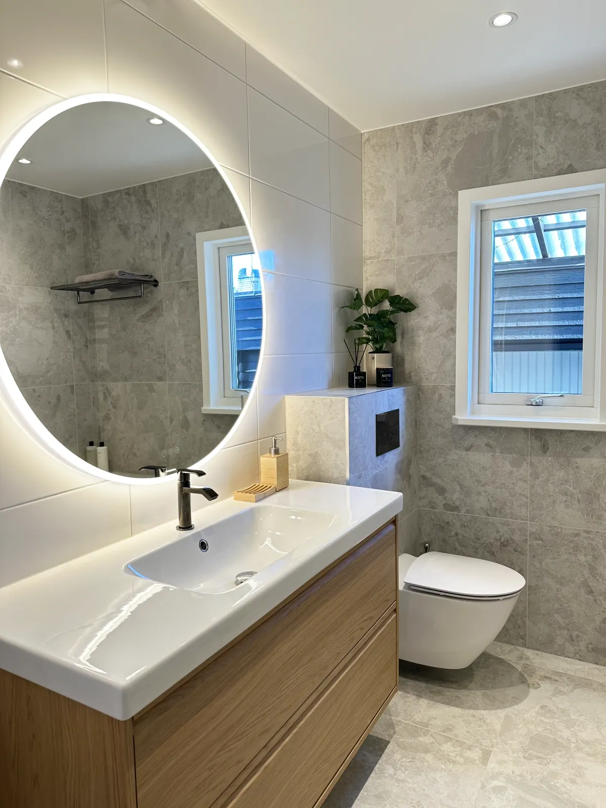 Modern badrumsrenovering i Järfälla med kommod och belyst rund spegel