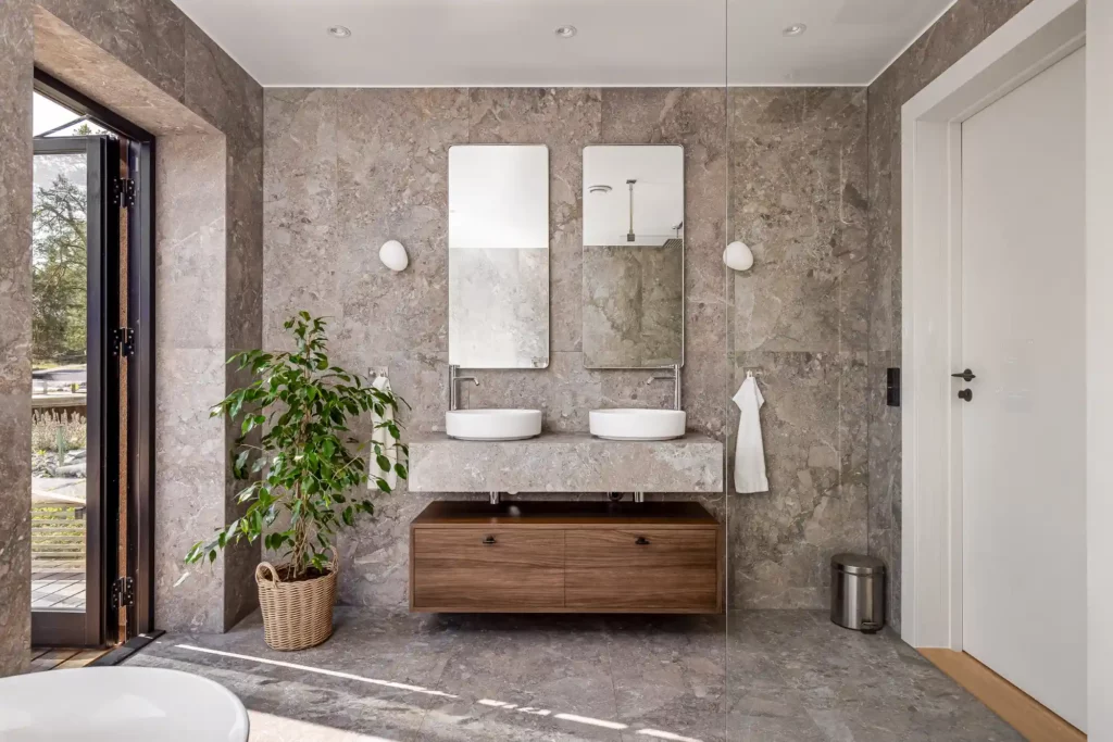 Modernt badrum i Stockholm med dubbla handfat, speglar, naturstensväggar och trädetaljer efter badrumsrenovering