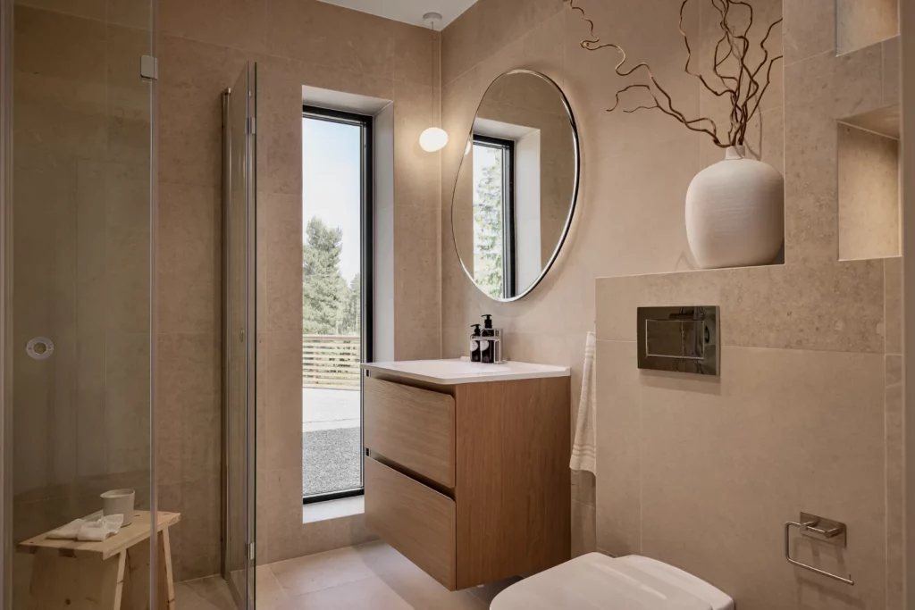 Modernt badrum i Stockholm med träkommod, rund spegel, stora fönster och stenklädda väggar efter badrumsrenovering i Stockholm